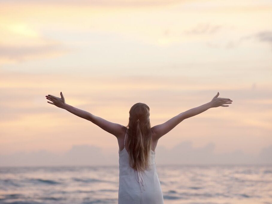 Rear View of Woman With Arms Raised at Beach during Sunset